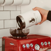 main qui verse des grains de café dans un moulin du machine espresso rouge